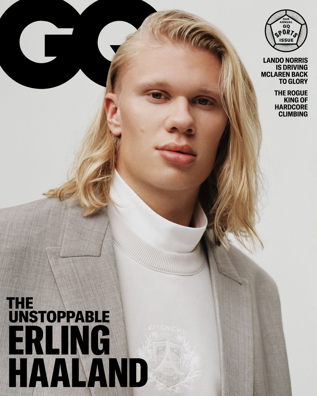 Close-up portrait of Erling Haaland on a magazine cover wearing a grey blazer, white top, and long blonde hair, against a light grey backdrop.