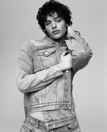 Monochrome portrait of a young man with curly hair wearing a denim jacket against a plain light background