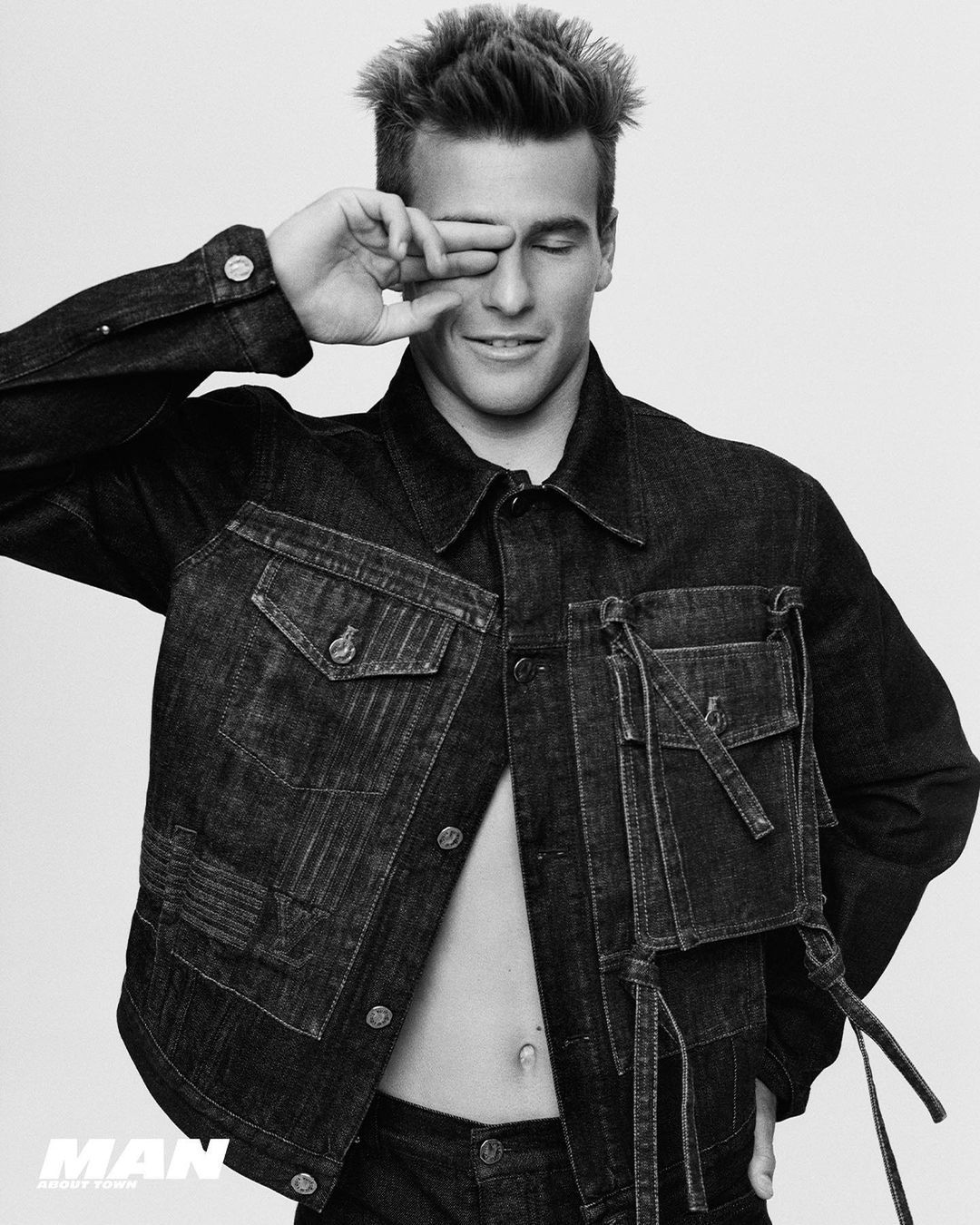 Black and white portrait of a young man wearing a dark denim jacket with his hand covering his eyes