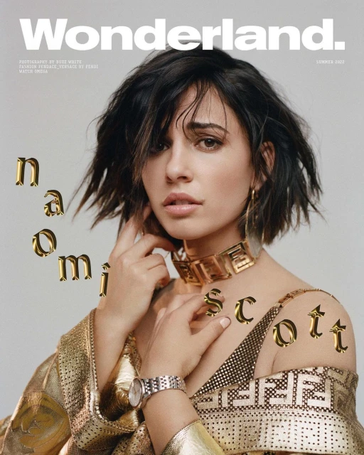 Naomi Scott on Wonderland Magazine cover with gold statement jewelry and graphic-patterned top, shot in a bright photo studio.