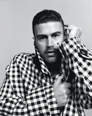 Portrait of a man in a black and white gingham patterned coat holding the collar up against a light grey background