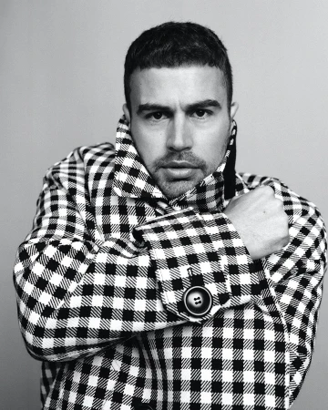 Man wearing a black and white checkered coat posing against a plain grey studio backdrop