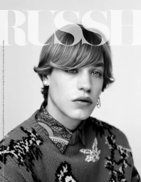 Black and white portrait of a young man wearing a patterned knit sweater and collared shirt with pearl earrings by Buzz White.