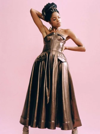 Black woman in a metallic bronze strapless structured gown posing against a solid pink background by Buzz White.