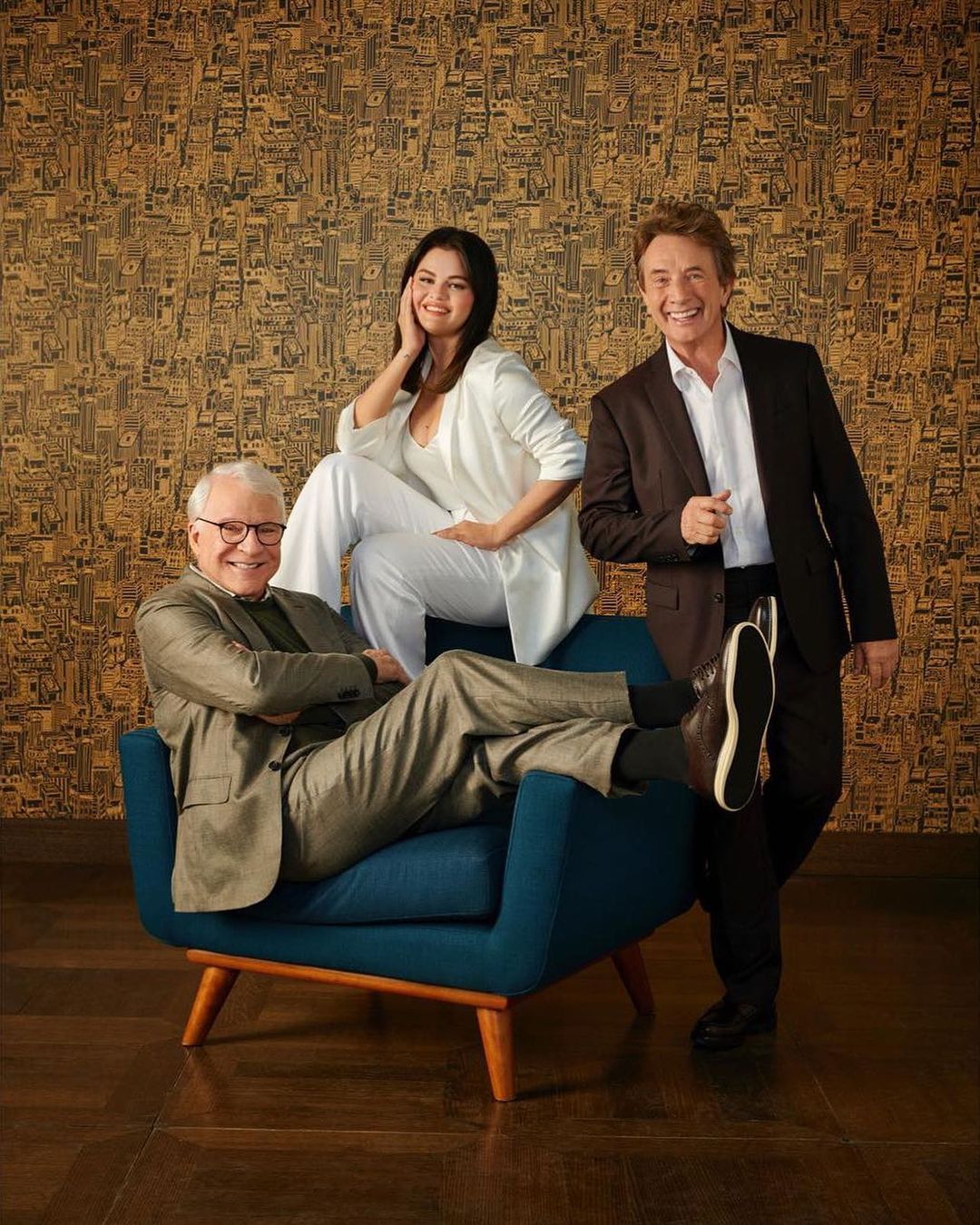 Three adult actors – Selena Gomez, Steve Martin, and Martin Short – pose in suits in an indoor portrait against a patterned backdrop.