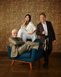 Steve Martin, Selena Gomez, and Martin Short posing together in a studio setting against a patterned gold wallpaper background.