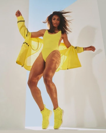 Ciara leaping in a bright yellow one-piece swimsuit and matching jacket against an architectural white backdrop