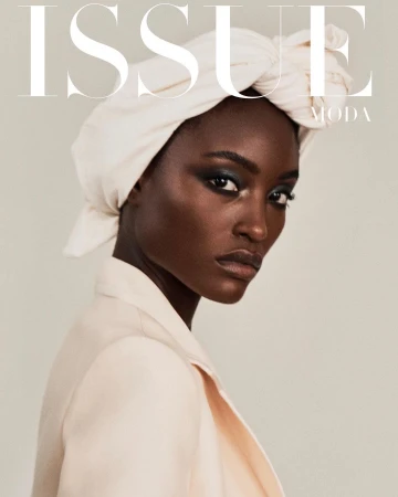 Black woman in a cream-colored headwrap and blazer posing against a solid light backdrop with magazine typography overlay