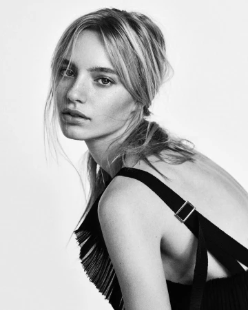 Monochrome portrait of a young woman with blonde hair in a black strap top against a white background.