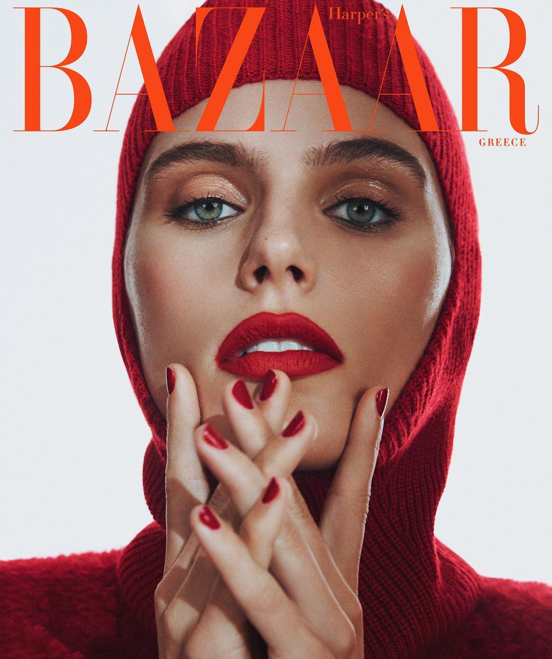Fashion magazine cover featuring a woman with bright red lipstick and matching knit hat, hands raised to her face in a close-up shot.