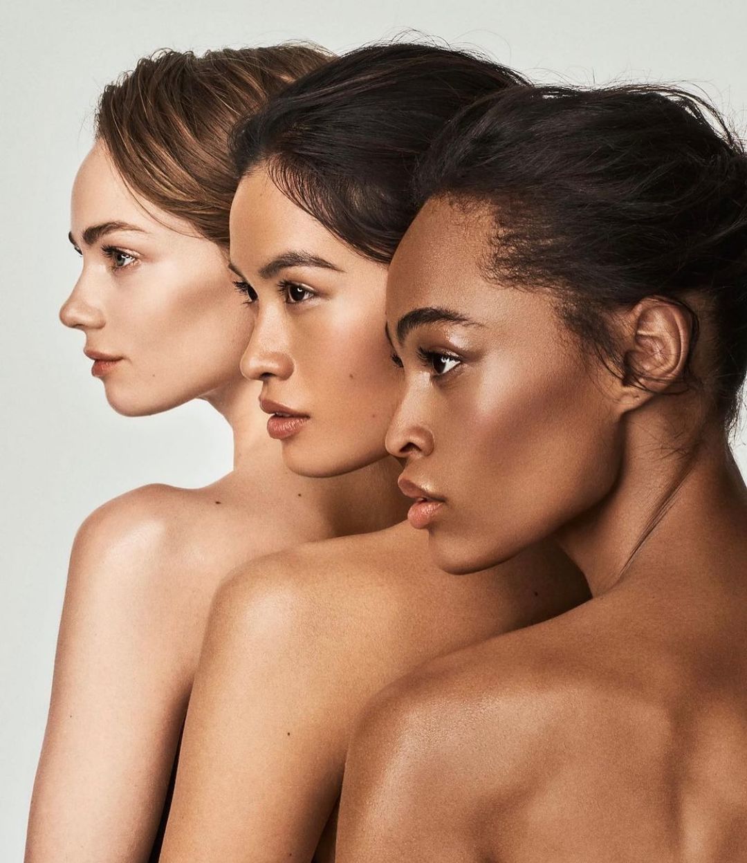 Close-up portrait of three women with different skin tones standing in a row, showcasing diverse beauty in a clean, studio setting.