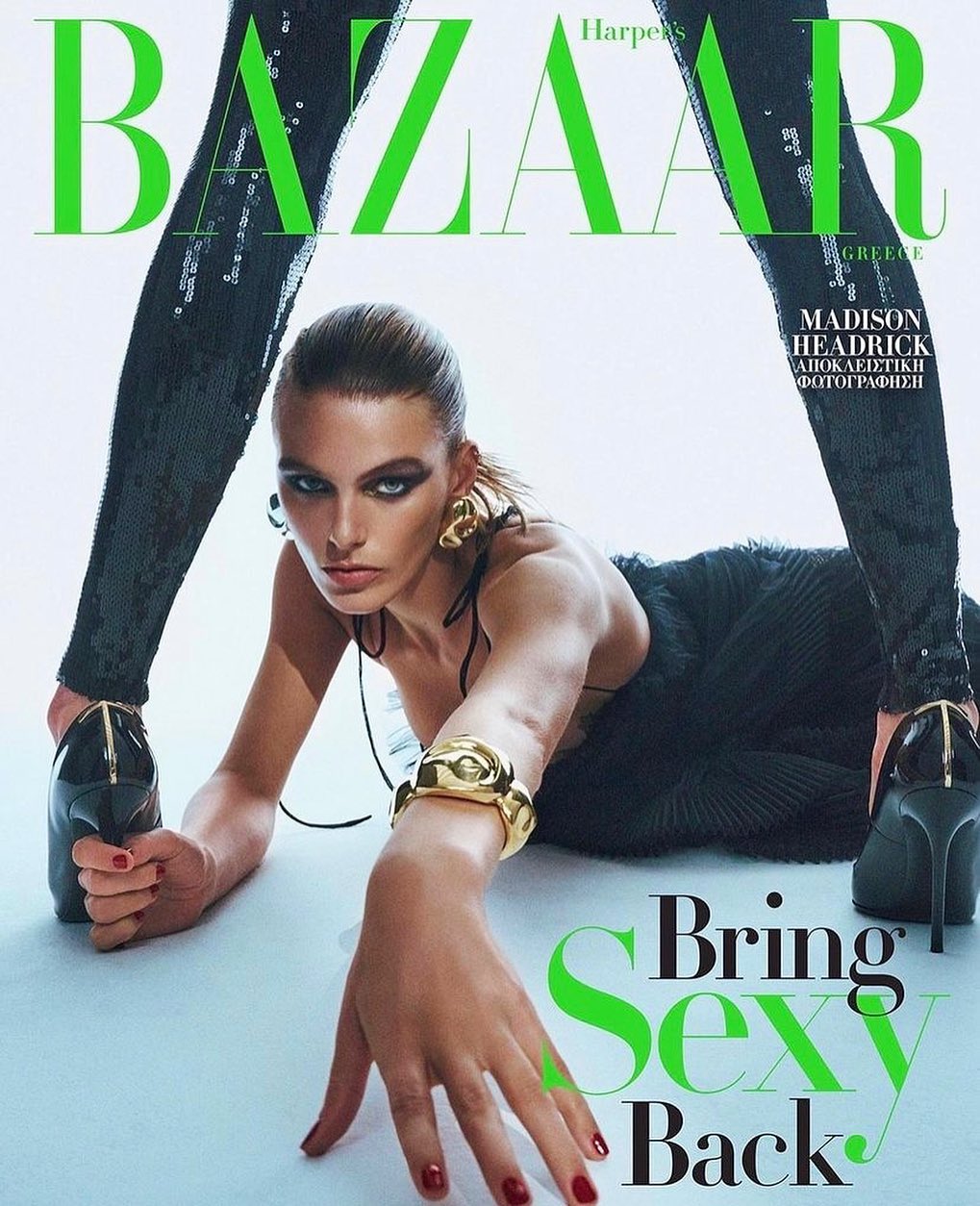 Fashion magazine cover featuring a model in a black dress with gold jewelry, posing against a white background with bold green typography.
