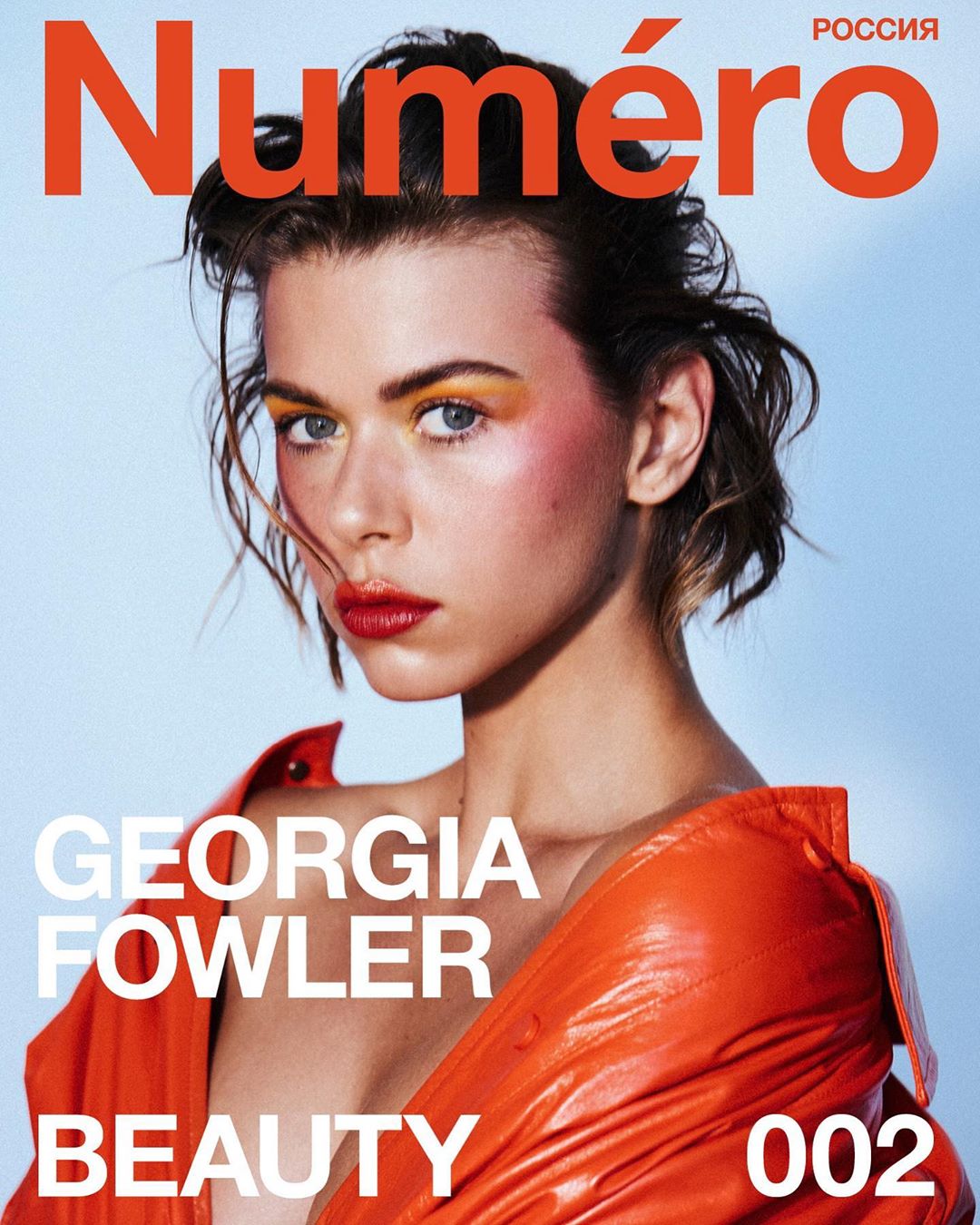 Magazine cover featuring a woman with artistic makeup and an orange jacket on a light blue background with prominent magazine text.