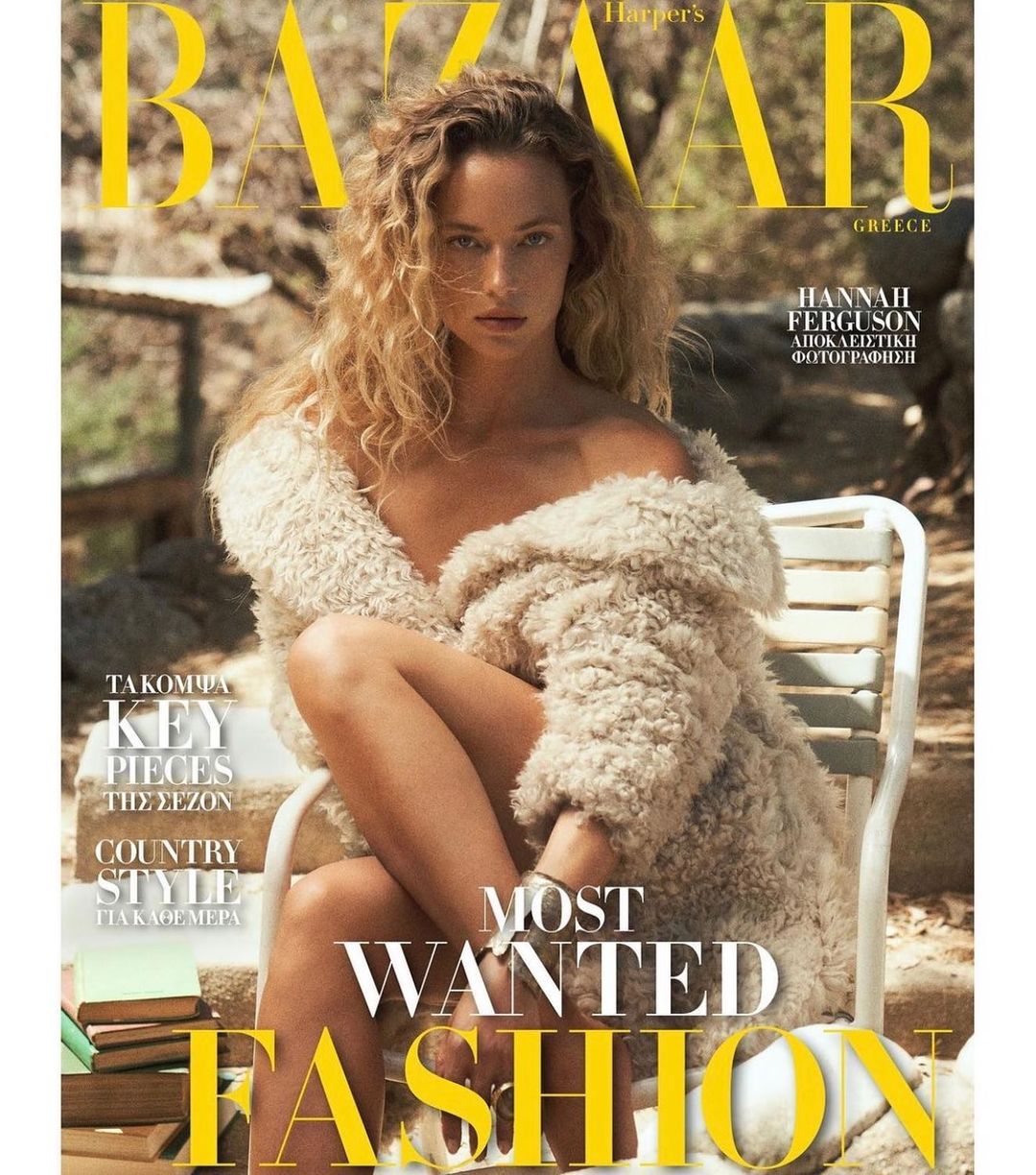 Fashion magazine cover featuring a curly-haired woman in a fur coat, sitting on a white chair, with a stack of books nearby.
