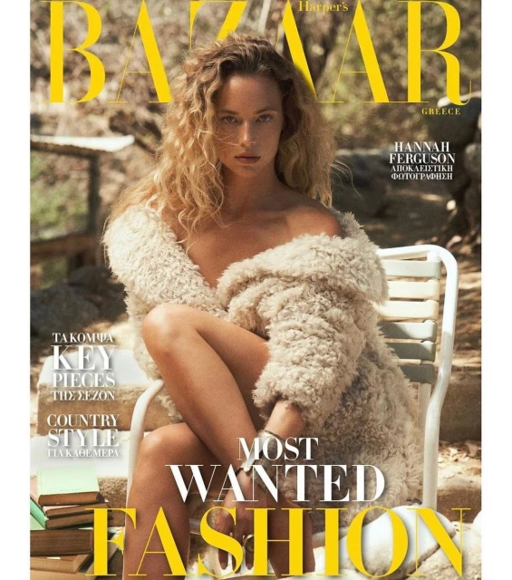 Fashion magazine cover featuring a curly-haired woman in a fur coat, sitting on a white chair, with a stack of books nearby.