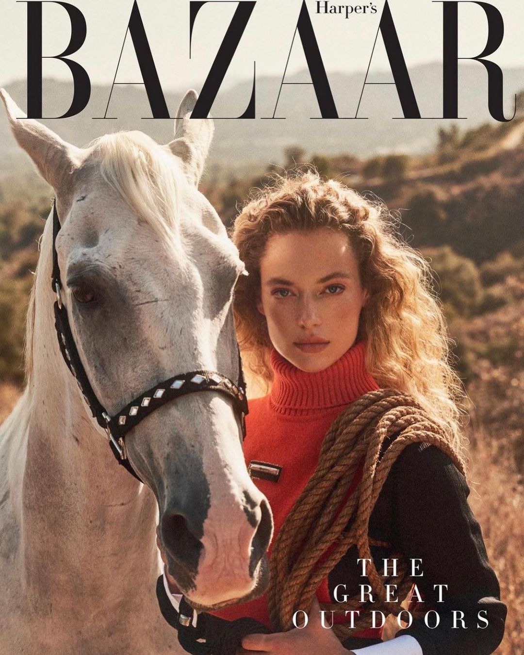 Fashion editorial magazine cover featuring a curly-haired model with a white horse against an outdoor, sunlit, natural background.