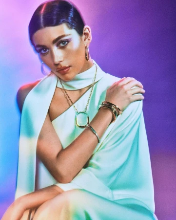 Woman in pale green satin dress wearing gold jewellery against a purple gradient background by Caleb and Gladys