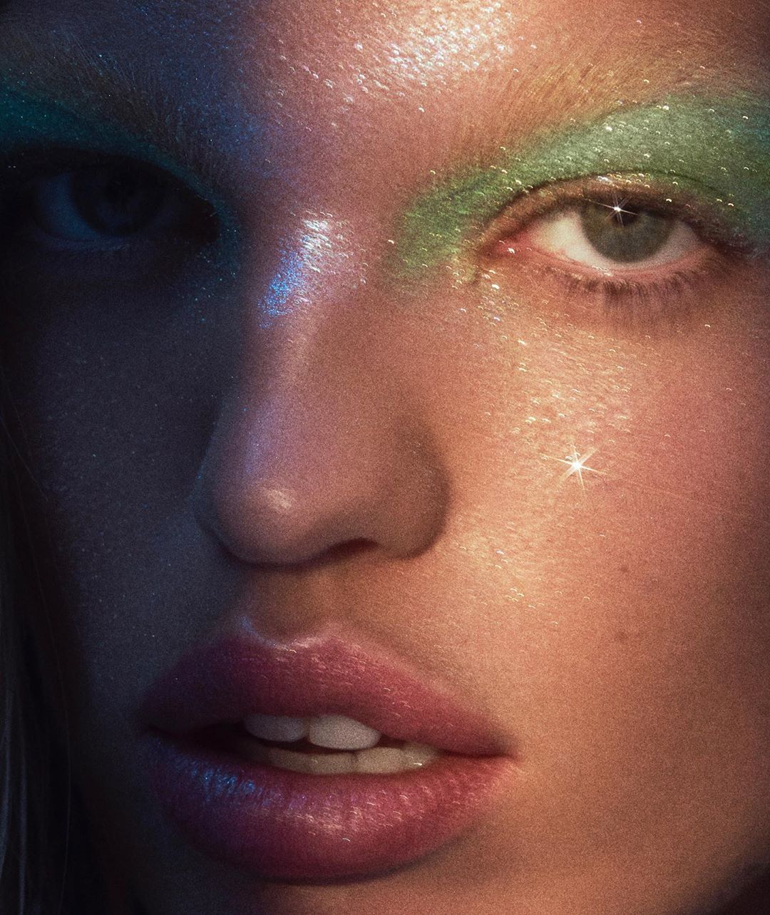 Close-up portrait of a female adult with creative green and glittering eye makeup. The image features soft, diffused lighting and cool tones.