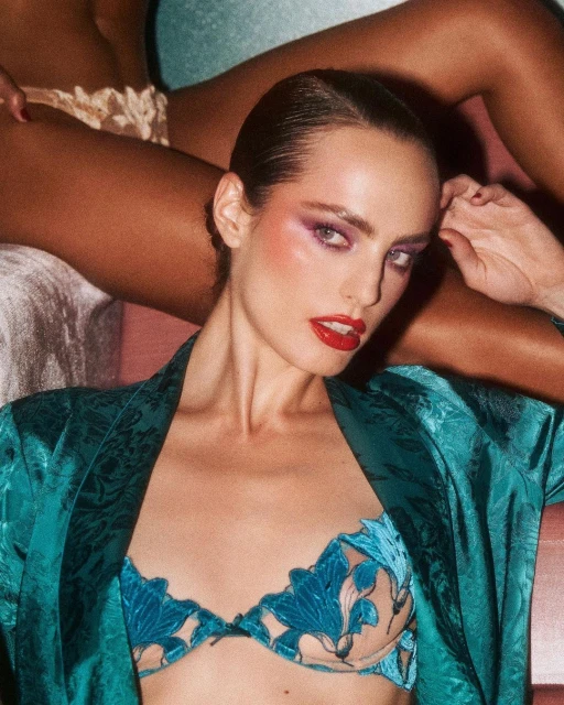 Close-up of an adult female model with red lipstick and purple eye shadow posing in a blue floral bra with a teal robe.