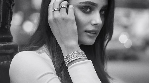 Monochrome close-up of a woman showcasing rings and multiple bracelets. The background is blurred with bokeh, indicating an outdoor urban setting.