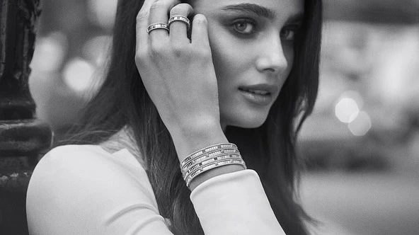 Monochrome close-up of a woman showcasing rings and multiple bracelets. The background is blurred with bokeh, indicating an outdoor urban setting.