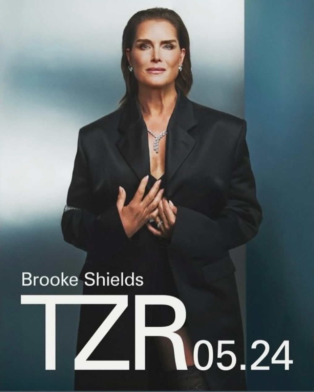 Brooke Shields poses in a dark blazer and jewelry against a blue background for TZR 05.24 fashion editorial portrait.