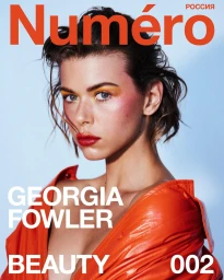 Portrait of a woman with vibrant yellow eye shadow and red lipstick wearing an orange leather top against a light blue background.