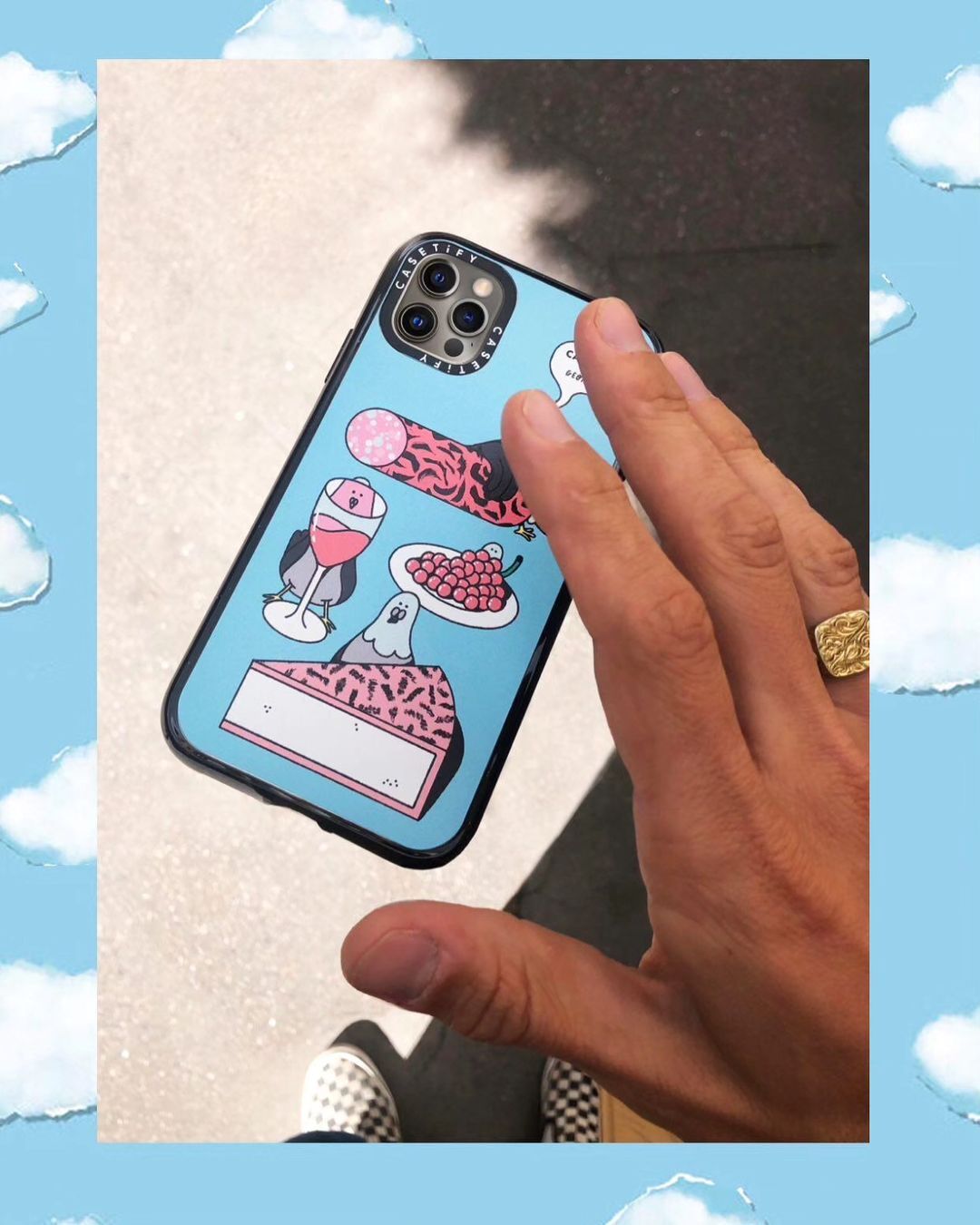Hand displaying a blue phone case with cartoon food designs, against an outdoor concrete surface with a hint of footwear visible.