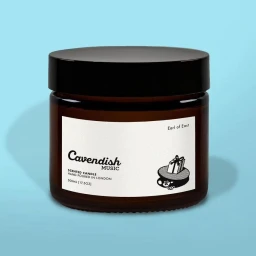 Amber glass jar candle with a black lid and white label against a light blue solid background.