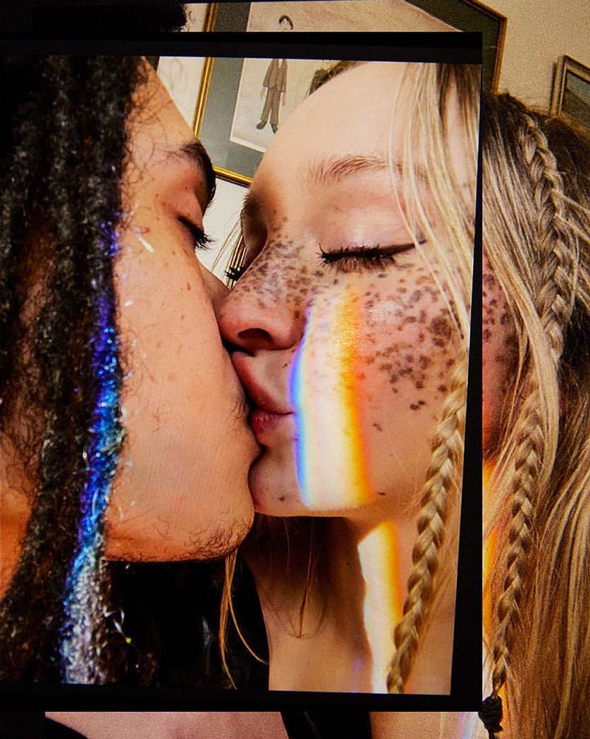 Close-up of a man and woman kissing, framed by a dark border with a rainbow light effect on their faces. 
