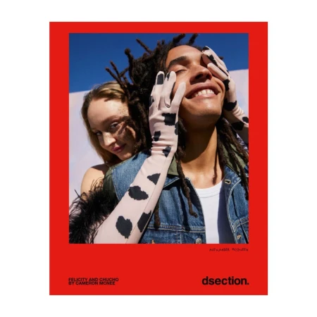 Fashion editorial featuring a smiling man with dreadlocks and gloves with a woman with blonde hair, set against a red and blue background.