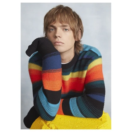 Portrait of a young adult male wearing a colorful striped sweater, resting his head on his hand, posing against a neutral background.