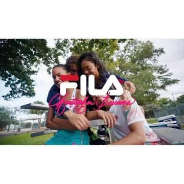 Four people of mixed ethnicities are outdoors sitting at a picnic table, embracing and smiling. They're wearing FILA branded apparel.