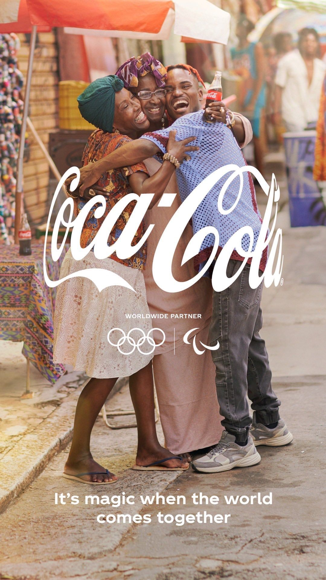 Coca-Cola advertisement featuring three individuals embracing in an outdoor market setting, promoting the Olympics worldwide partnership.