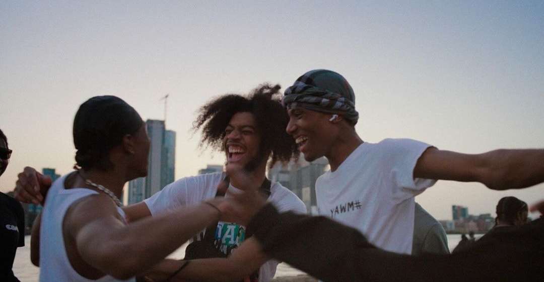 Outdoor gathering of young adults laughing against an urban backdrop during daylight. Several people are partially in the frame.