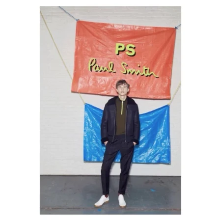 Male model wearing dark jacket and pants, standing in front of a backdrop with the 'Paul Smith' logo in an indoor setting.