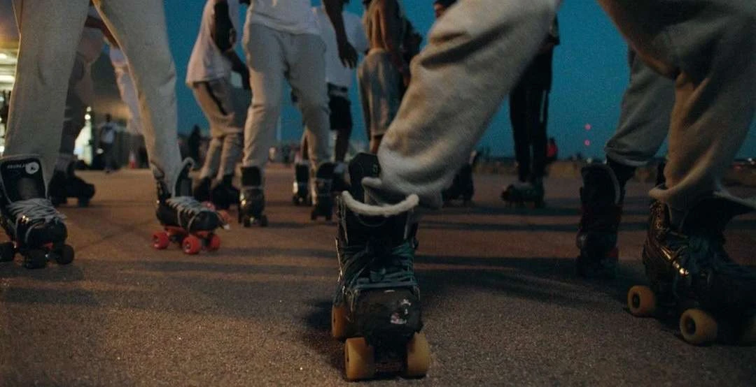 Group of people wearing roller skates on an outdoor paved surface at dusk, focus on the roller skates and legs of the skaters.
