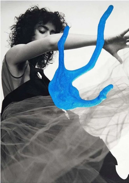 Artistic black and white portrait of a woman with curly hair and an open-armed pose juxtaposed with a digitally added bright blue sculpture.