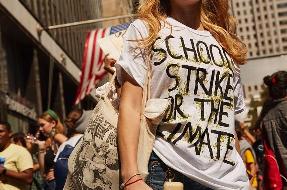 A person wears a 'School Strike for Climate' t-shirt at an outdoor demonstration, accessorized with a tote bag, standing in a crowd.