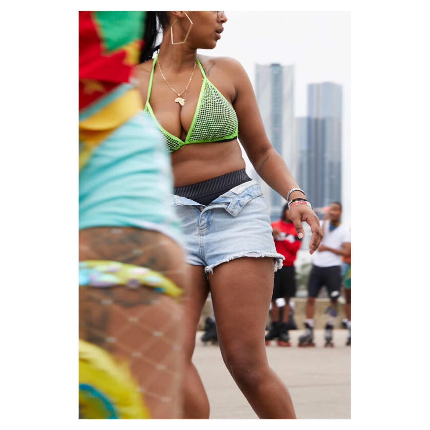 Two women on roller skates outdoors on a sunny day, wearing colorful summer clothes, with city buildings in the distance, medium shot.