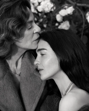 Intimate black and white portrait of two women in soft focus with a rose bush backdrop, showcasing a tender moment in natural light.