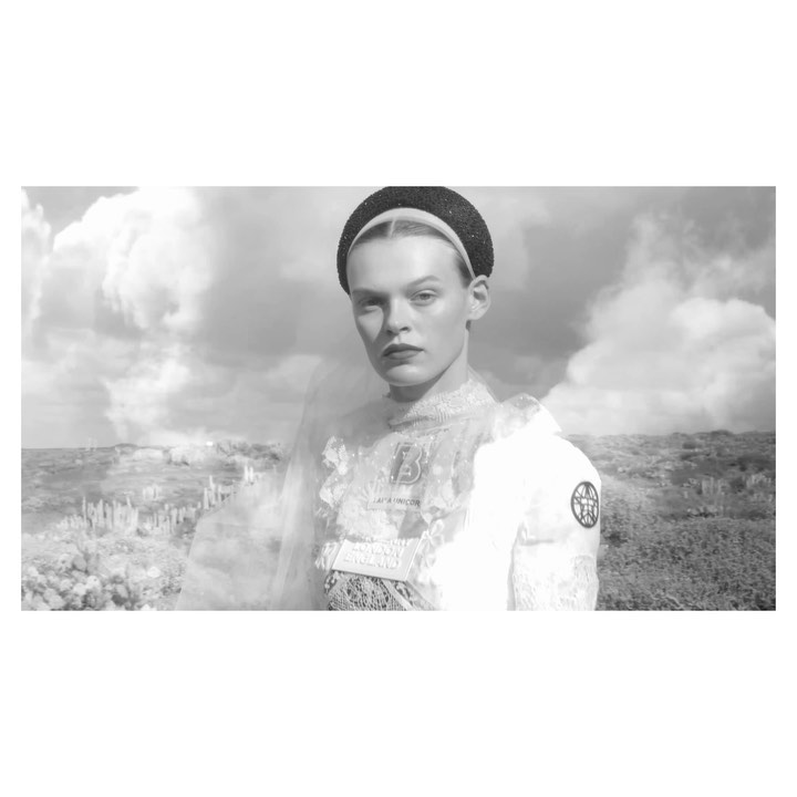 Monochrome portrait of a female model wearing a textured headband and patterned top against an outdoor sky background