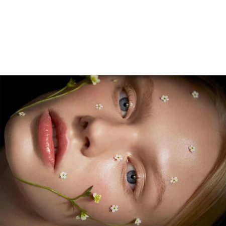 Close-up beauty portrait of a woman with delicate small white flowers placed across her face and a green stem framing her cheek, by photographer Camilla Akrans.