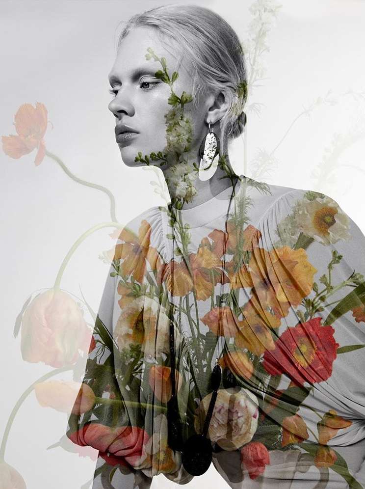 Artistic fashion portrait of a woman with floral dress and botanical overlay on a white backdrop, earring detail.