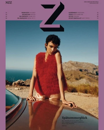 Model in a red fuzzy top leaning against a car hood with a coastal mountain range in the background
