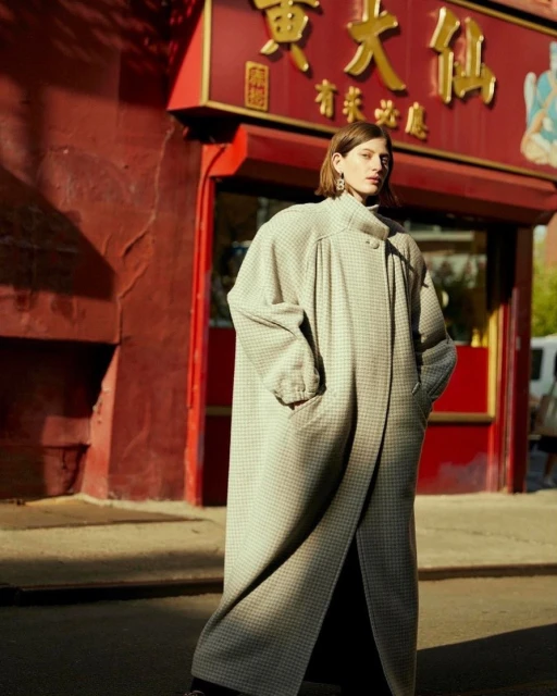 Fashionable woman in oversized checkered coat posing on city street in front of Chinese restaurant with bright red architectural details.