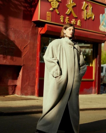 Fashionable woman in oversized checkered coat posing on city street in front of Chinese restaurant with bright red architectural details.