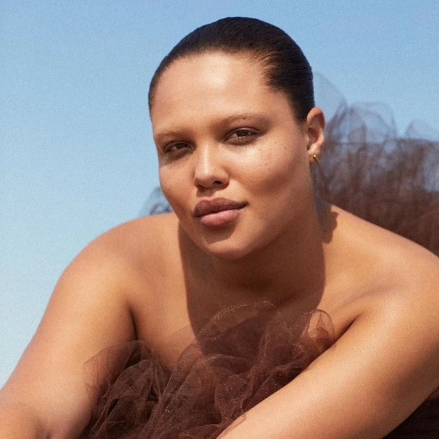 Portrait of an adult woman with brown tulle. The backdrop is a gradient of blue sky, shallow depth of field and natural lighting.