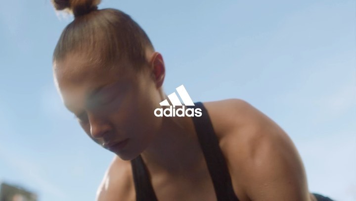 A woman in workout gear is captured in a low-angle shot against a bright sky, featuring the Adidas logo prominently.