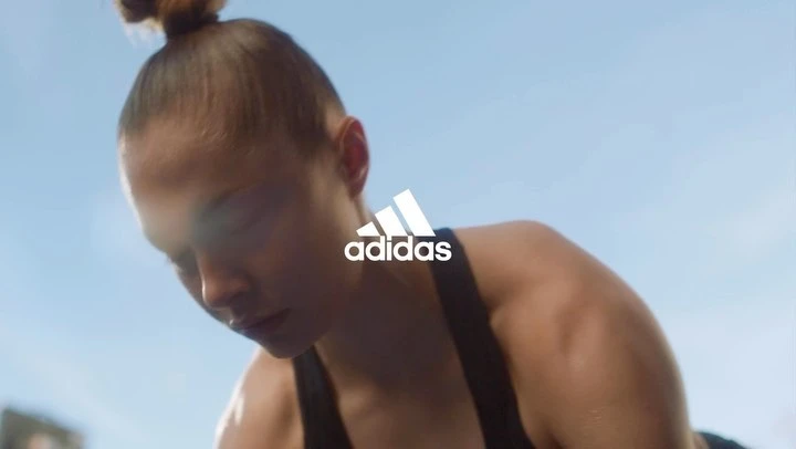 A woman in workout gear is captured in a low-angle shot against a bright sky, featuring the Adidas logo prominently.